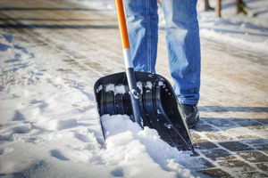 man with snow shovel clearing brick sidewalk