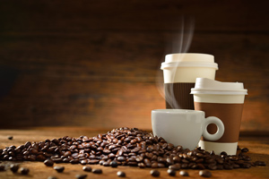 steaming coffee cups sitting in coffee beans